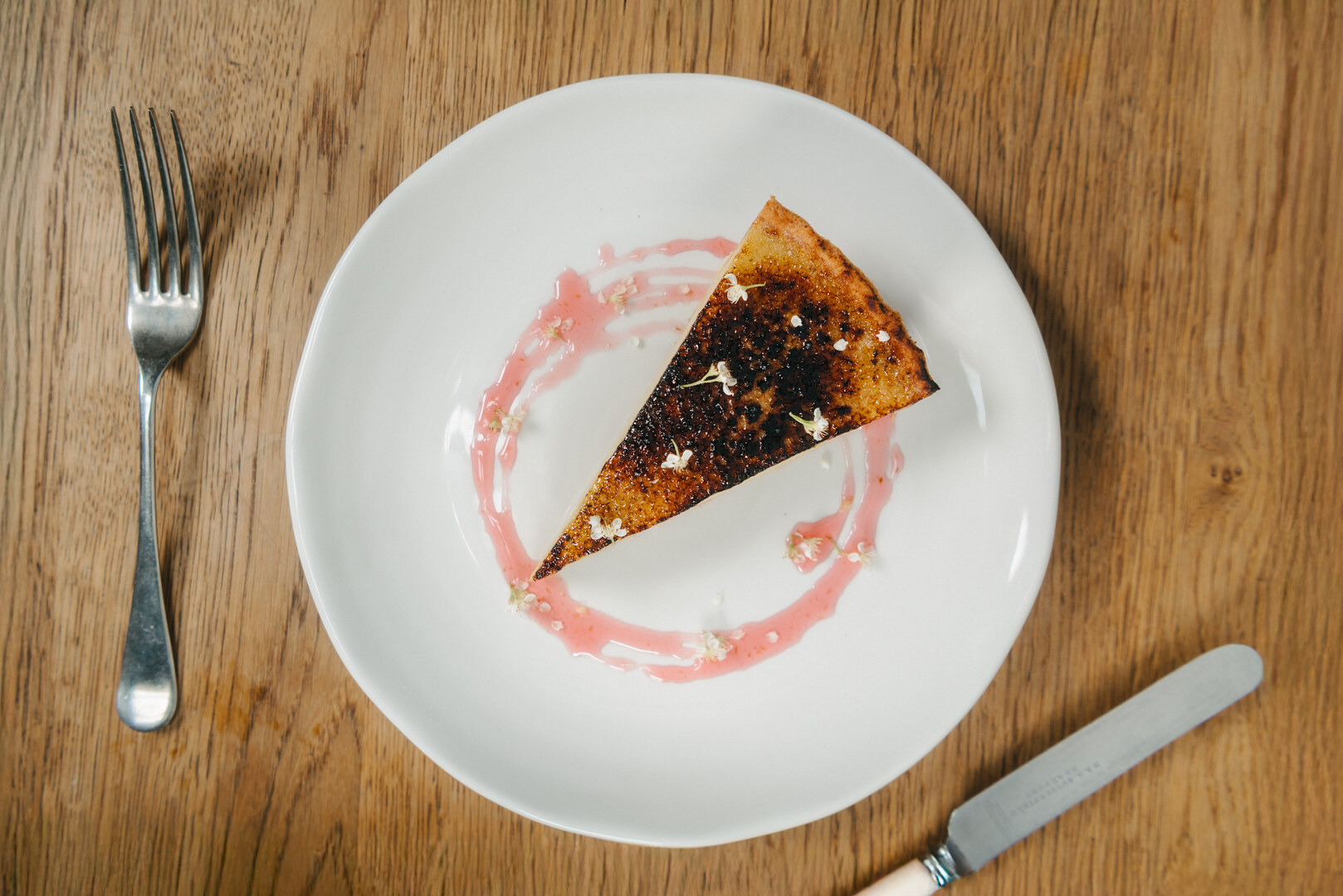 Slice of burnt custard tart with pink sauce and flowers.
