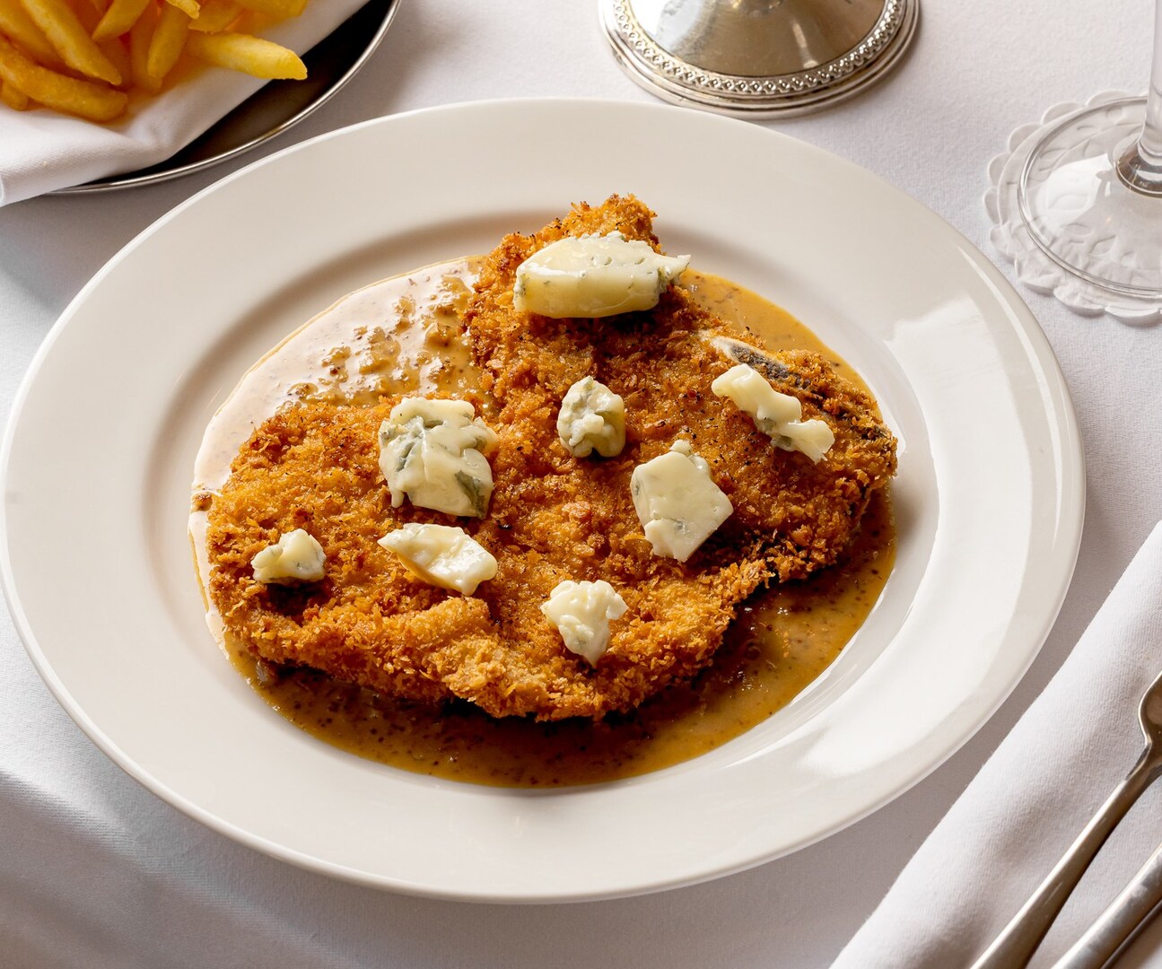 Schnitzel with blue cheese and sauce, served with french fries.