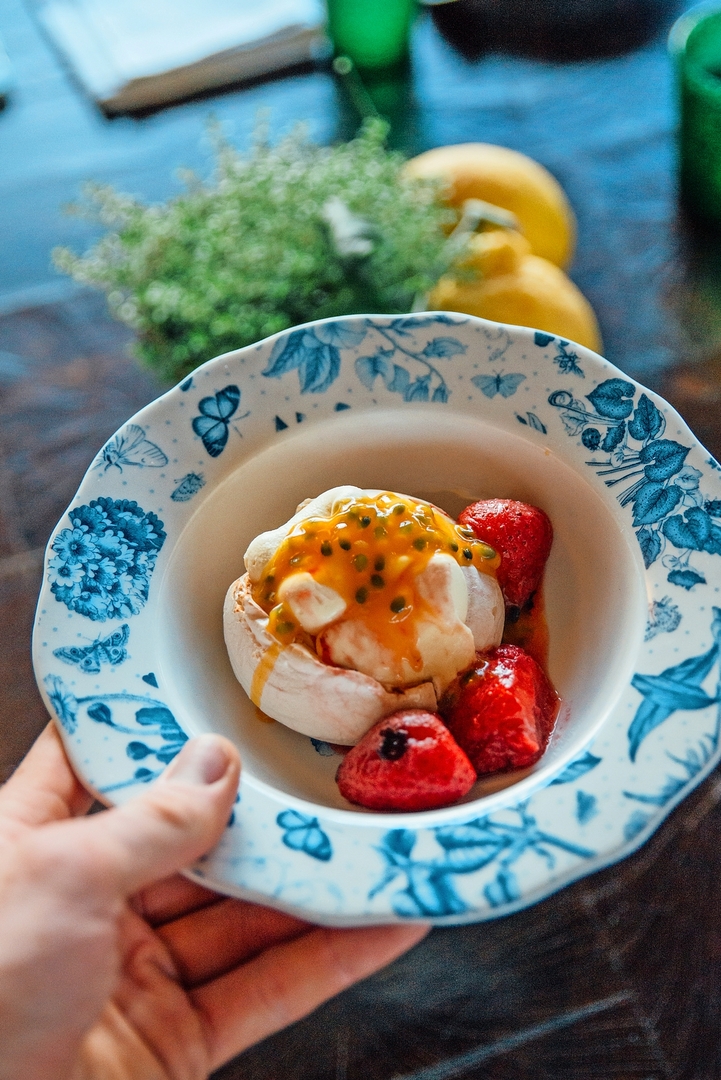 Pavlova with passion fruit and strawberries on a decorative plate.