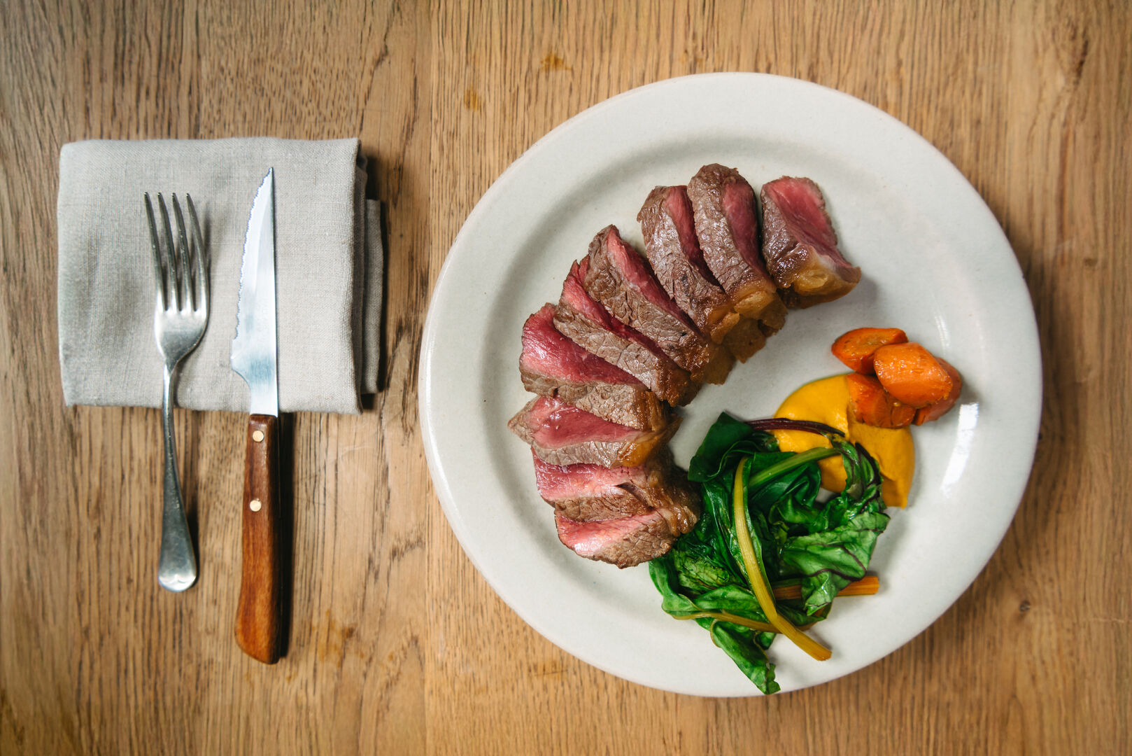 Sliced steak with carrots, chard, and a yellow sauce.