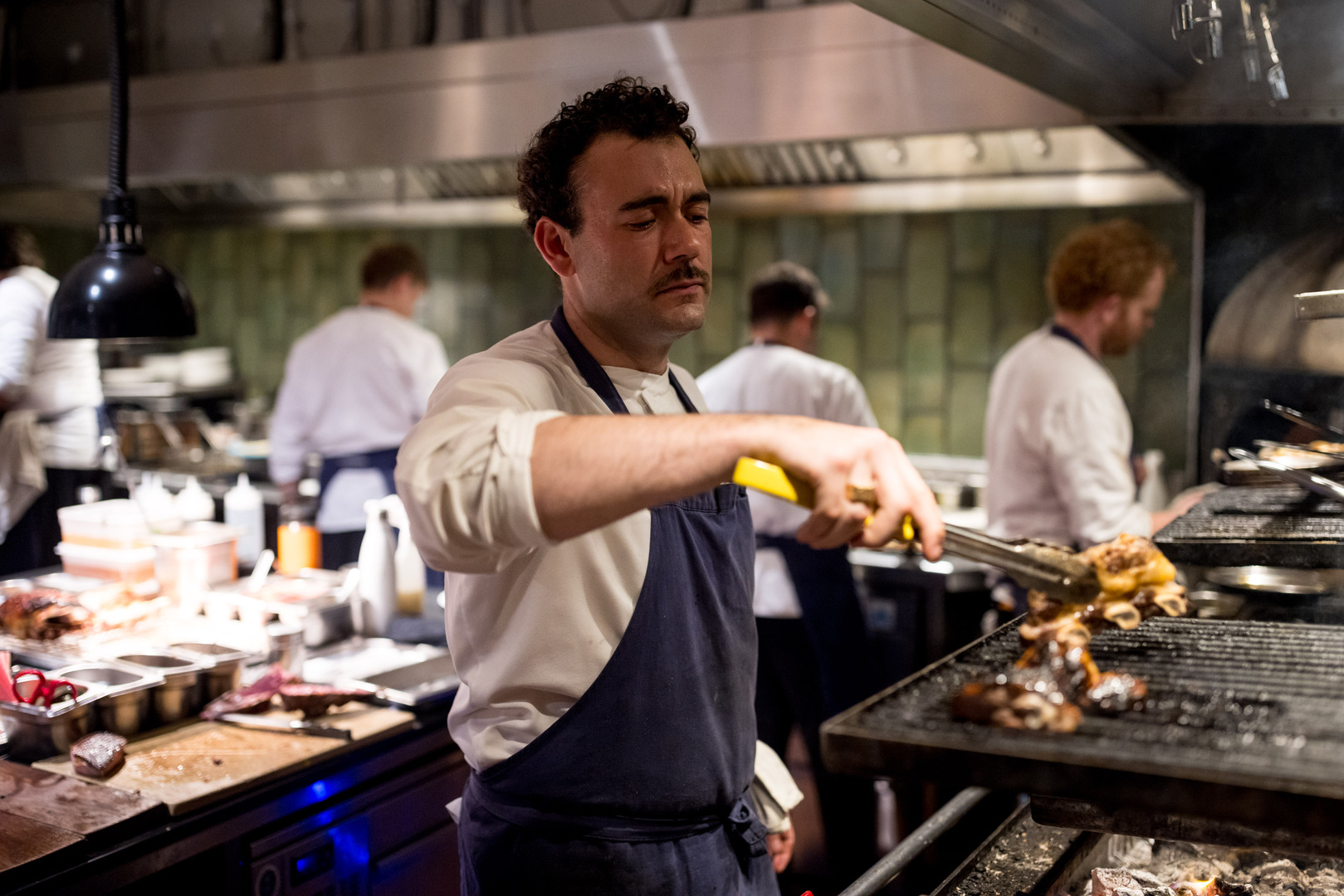 Chef grilling meat in a restaurant kitchen.